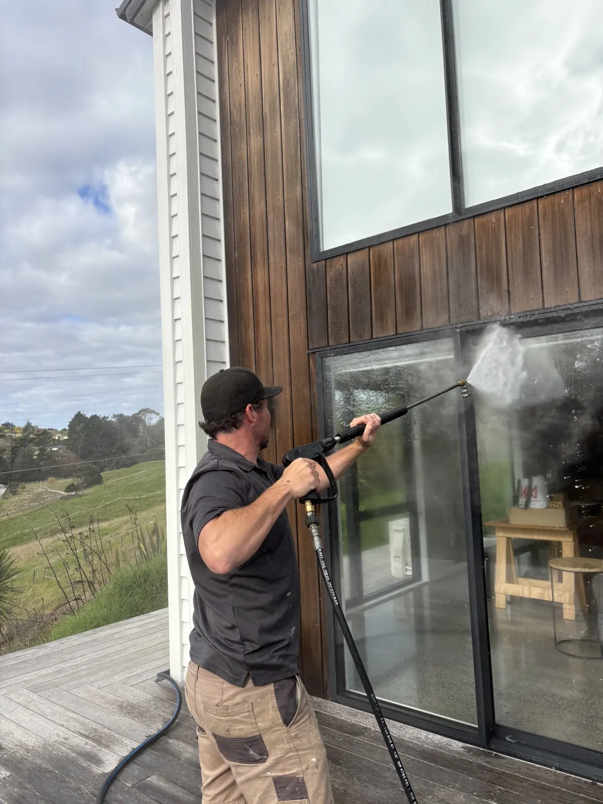 Technician soft washing stained cedar cladding and windows on a rural West Auckland home