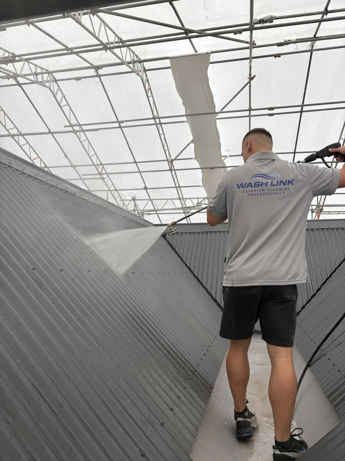 Low-pressure spray fanning across a corrugated metal roof during a roof wash